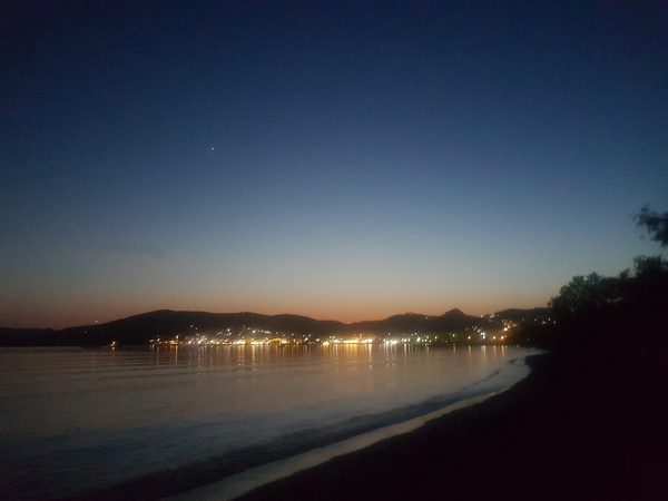 The port town of Adamas lit up at dusk around its wide curving bay on Milos