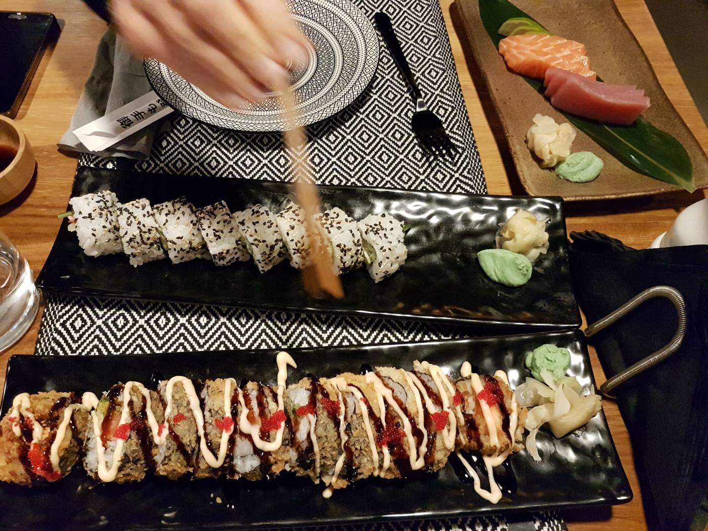 Sushi rolls, sashimi, wasabi and pickled ginger on black plates at a Pollonia waterfront restaurant in the evening