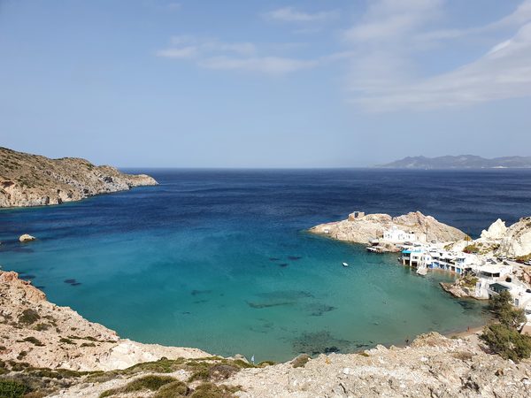The sheltered turquoise bay at Firopotamos, Milos, with its small beach, white chapel on the point and a cluster of syrmata boat garages along the shore
