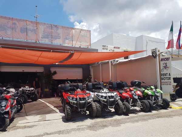 A row of rental ATVs and scooters lined up outside a Milos rental shop