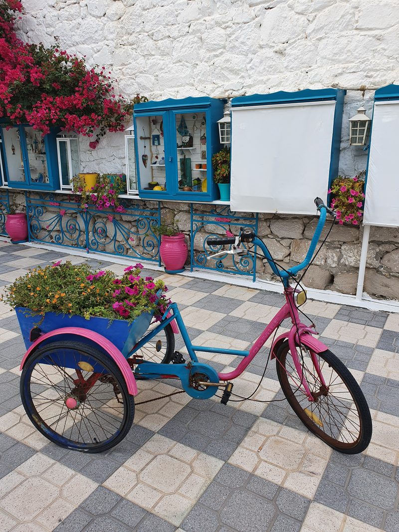 A flower-lined whitewashed alley in Adamas, with a painted bicycle outside a shop front