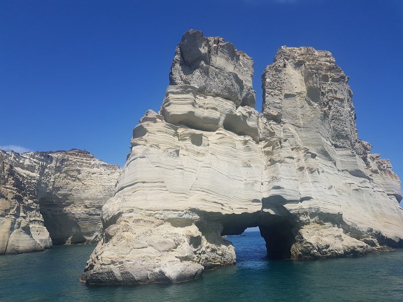 A massive pale sea stack at Kleftiko, split by a natural arch, seen close from the water