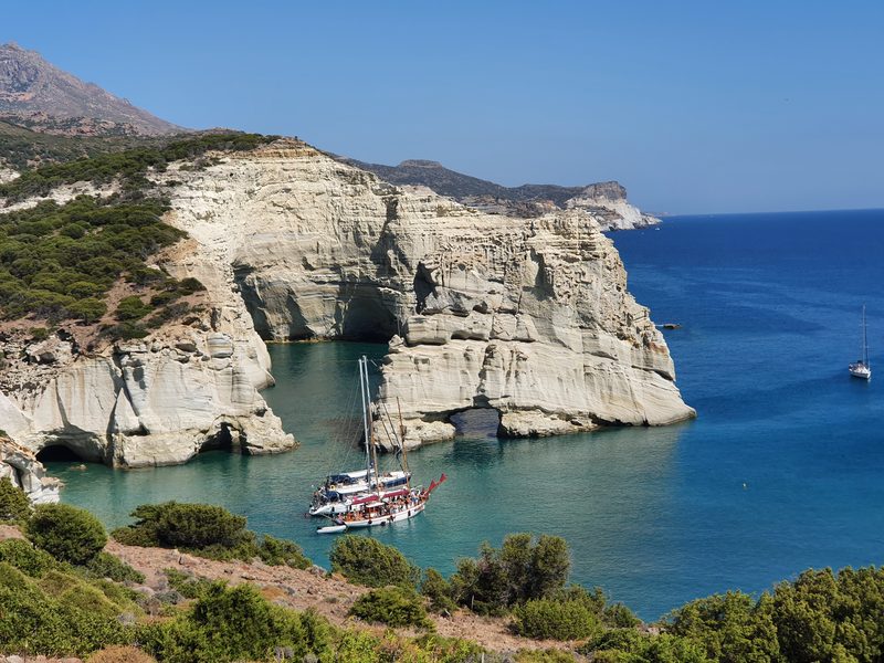 A traditional tour boat anchored in a turquoise inlet at Kleftiko, framed by tall white rock arches