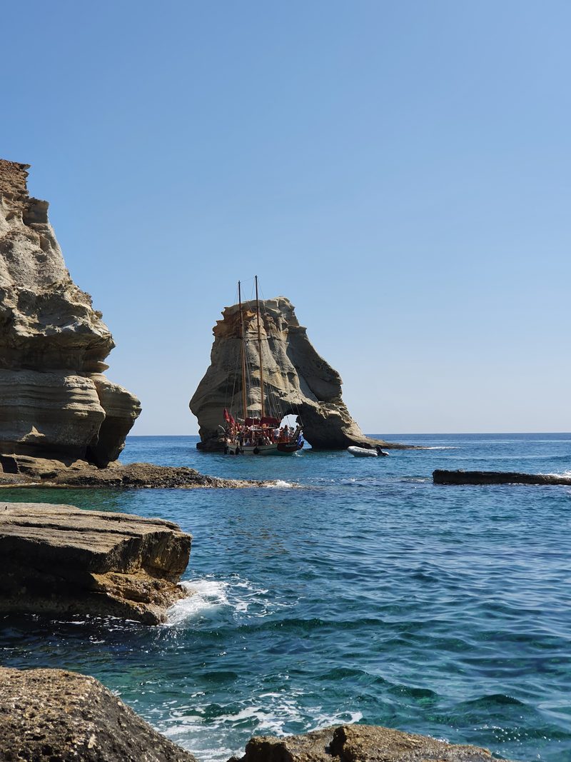 The prow of a tour boat passing close to a Kleftiko sea stack, with passengers gathered on deck