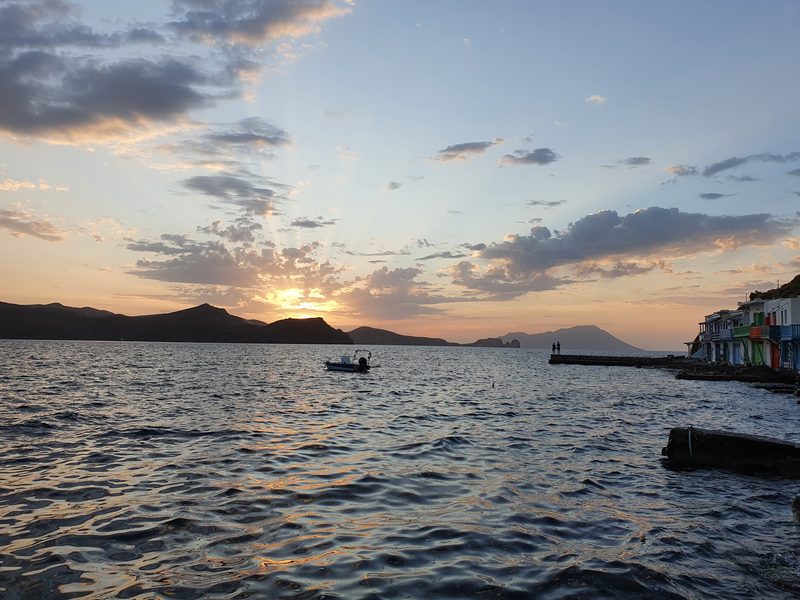 A wide sunset over the sea west of Milos, sunbeams breaking through cloud above silhouetted headlands