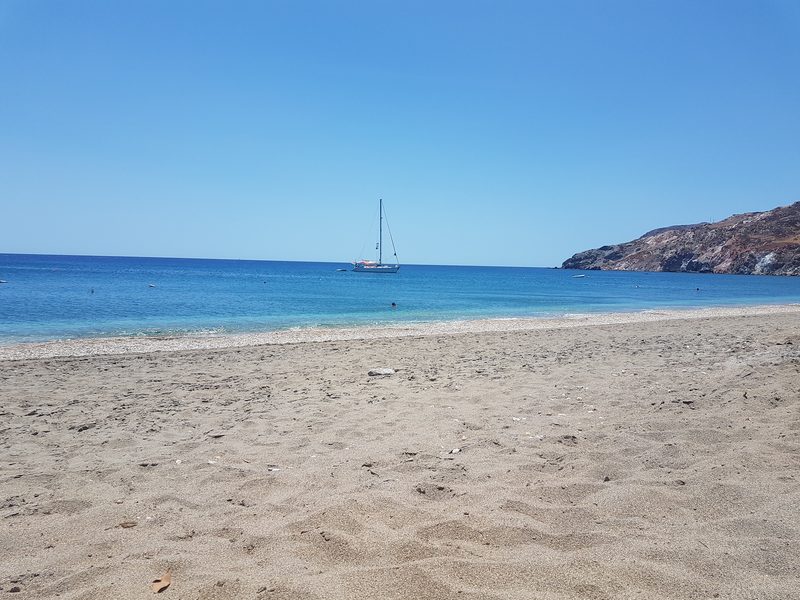 The pale sandy shore of Paleochori beach with a sailboat anchored in the clear water beyond