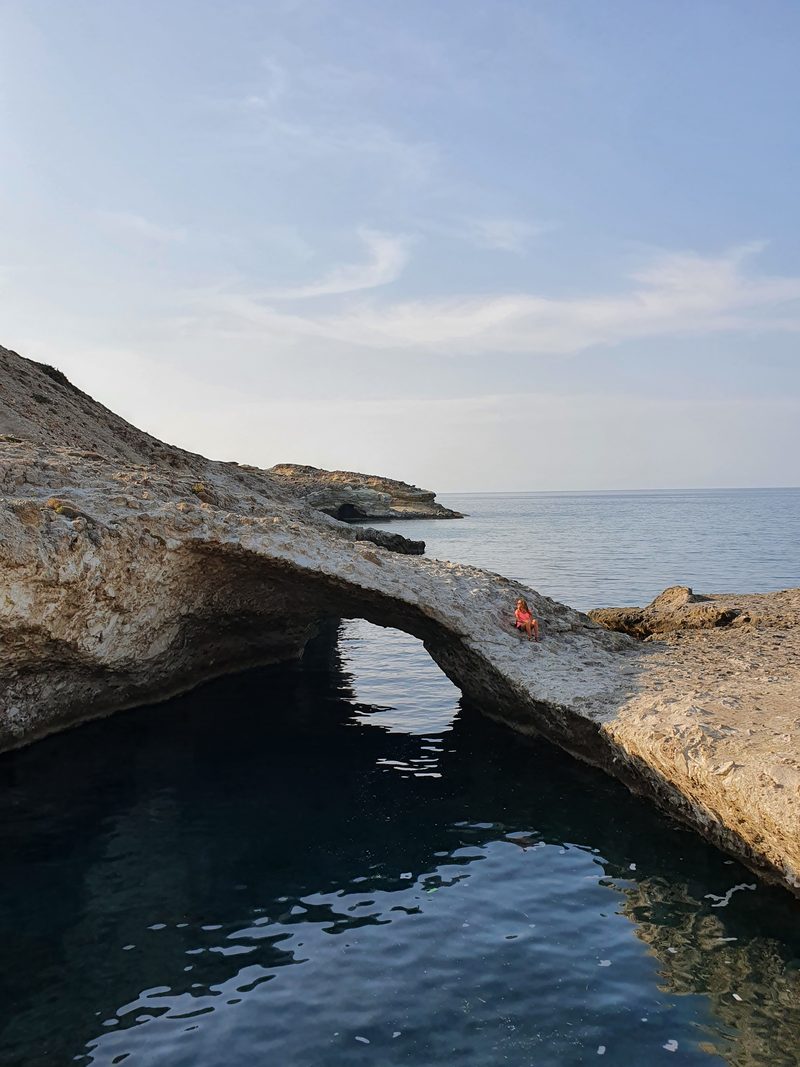 A swimmer on the pale rock beside the sheltered pool inside the narrow sea cave inlet near Pollonia
