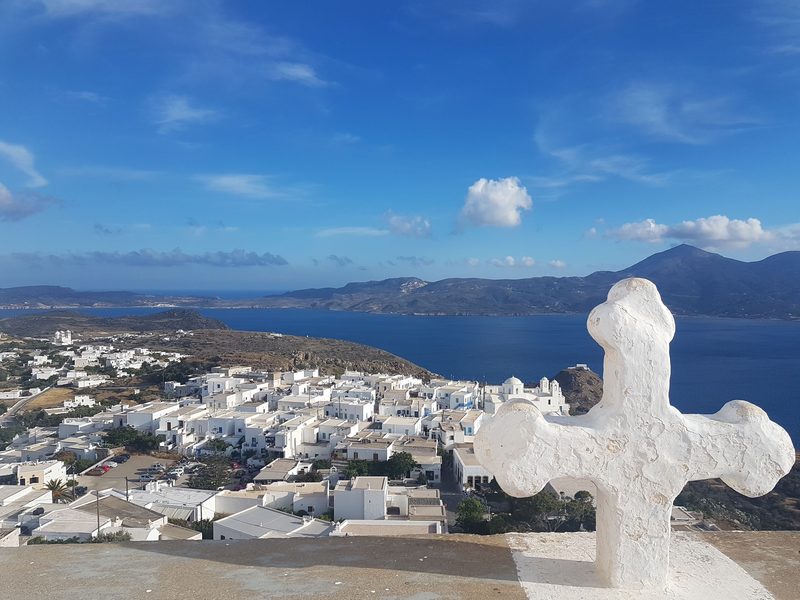 A whitewashed cross at the top of the Kastro climb, with Plaka's rooftops and the sea stretching out below