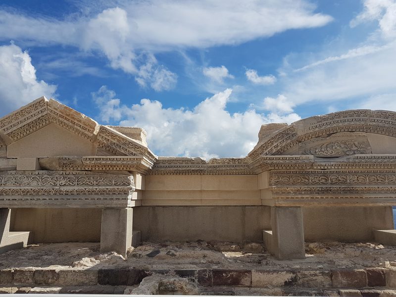 Ornately carved marble entablature and pediment fragments at the Trypiti ancient theatre against a blue sky