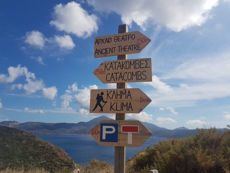 A wooden signpost pointing the way to the Ancient Theatre, the Catacombs and Klima above Trypiti, Milos