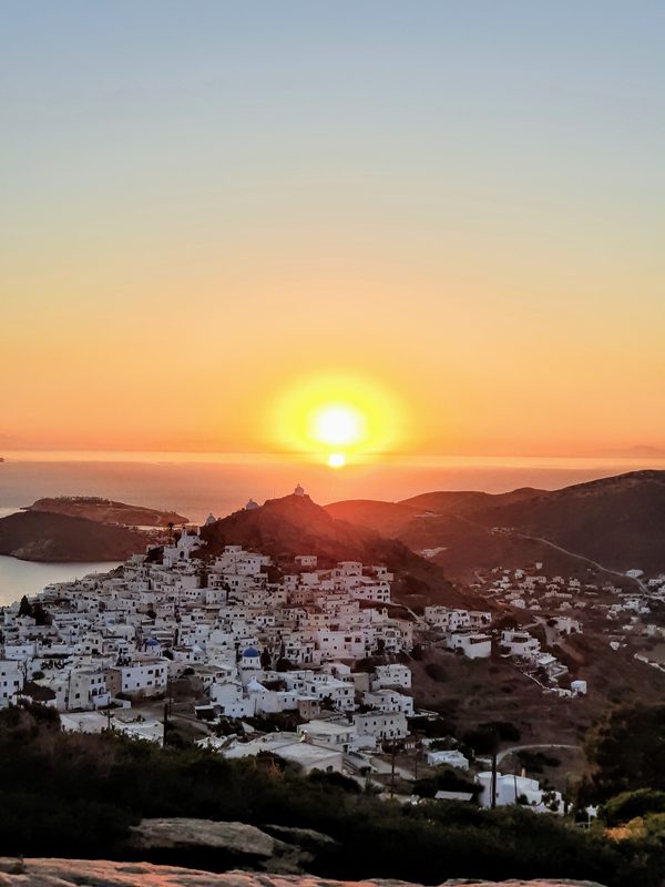 Sunset over Ios Chora, whitewashed houses on the hillside with a windmill silhouette against the glowing sky