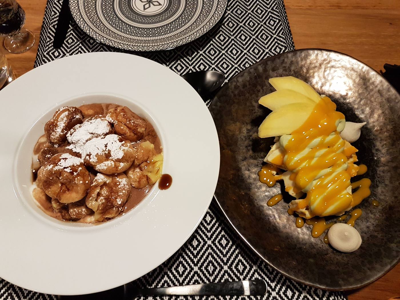 Two dessert plates, loukoumades and a mango dessert, served at a Milos restaurant table