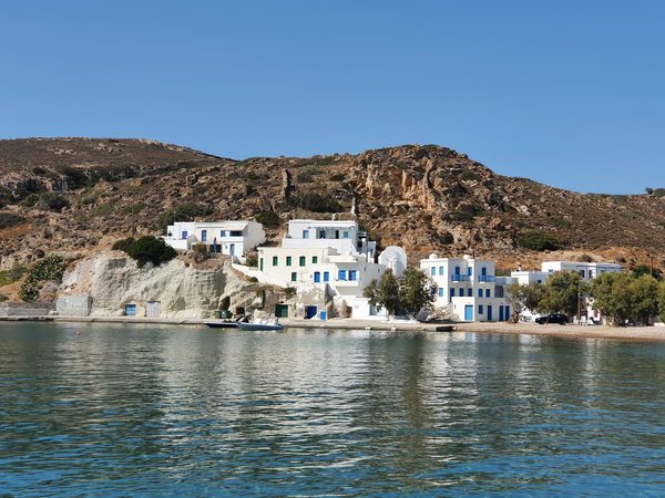 The small port of Psathi on Kimolos, a cluster of whitewashed houses on a rocky rise with the island's hills behind