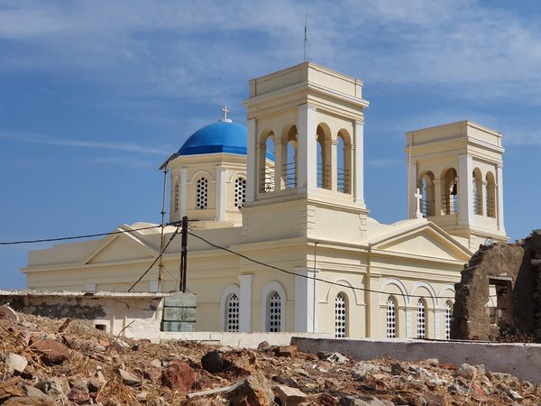 A blue-domed church with twin bell towers rising above ruined stone walls in Kimolos Chorio village