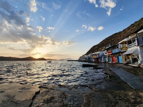 The colourful row of syrmata boat houses at Klima, Milos, lit by a low sunset with the cliff rising behind