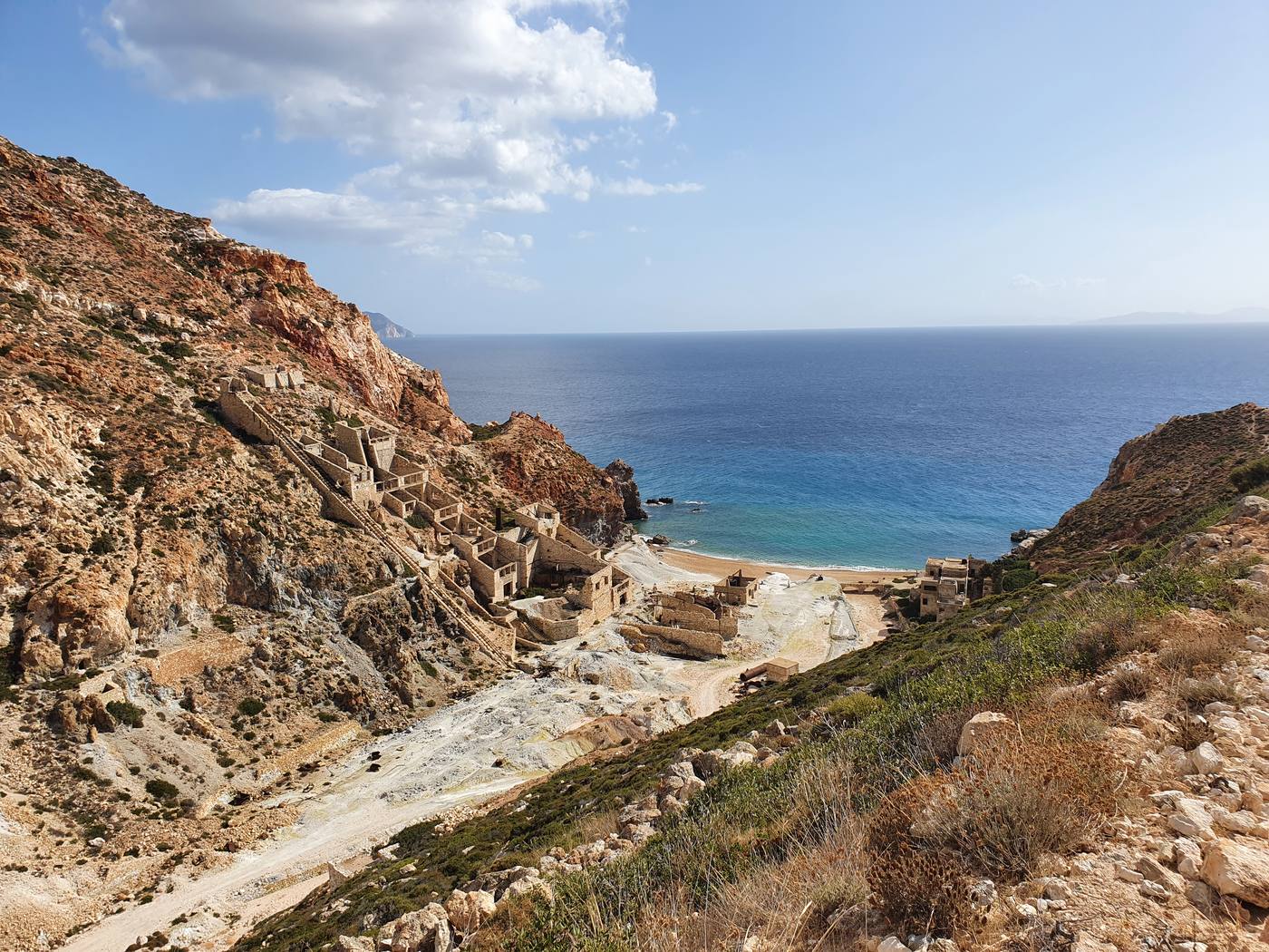 The abandoned Paliorema sulphur mine on Milos, ruined stone buildings and rusted cable lines on ochre-stained cliffs above the sea