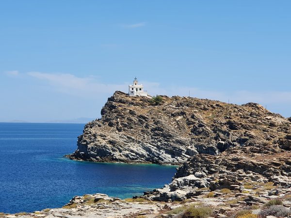 A whitewashed lighthouse standing on a rocky headland above the sea on Paros