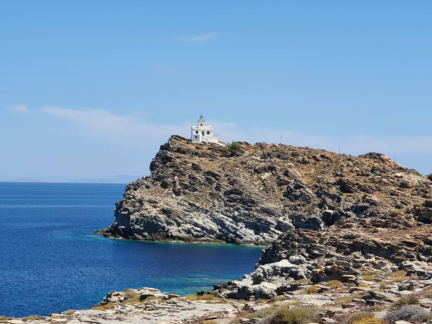 A whitewashed lighthouse standing on a rocky headland above the sea on Paros