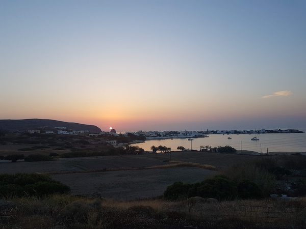 An elevated view over Pollonia harbour at sunset, with boats at anchor and the sun setting behind the headland