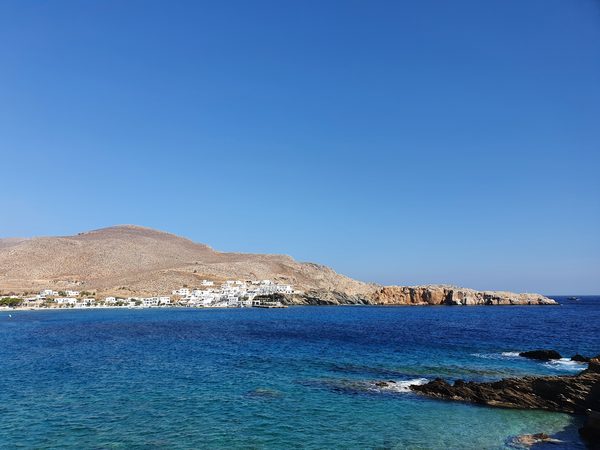 The whitewashed village of Folegandros seen from the water, houses along the shore beneath a dry hillside