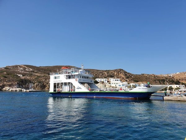 The small local ferry docked at Psathi port on Kimolos, with the whitewashed village behind it