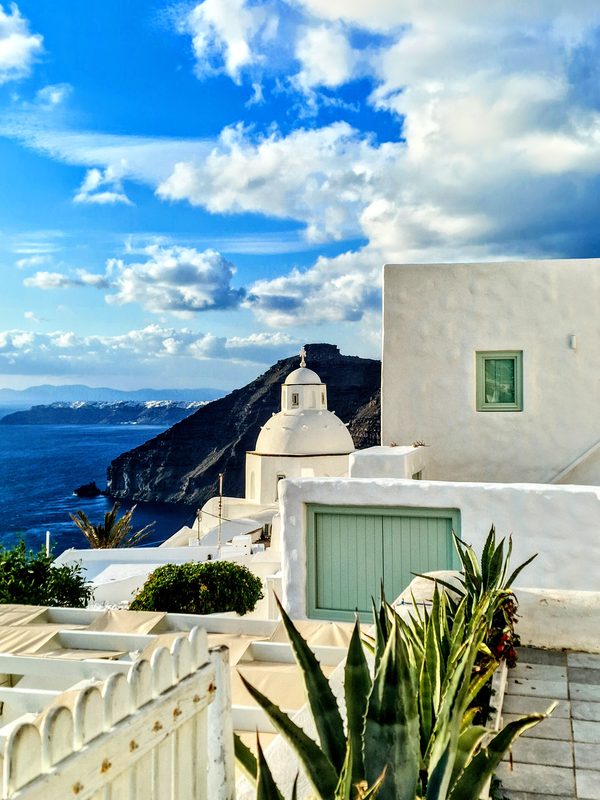 A blue-shuttered church dome above the Santorini caldera, whitewashed walls against the sea below