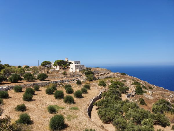 A whitewashed monastery and bell tower perched on a Sifnos headland above the sea