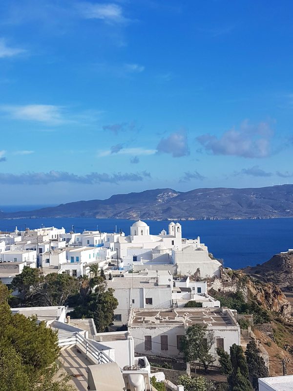 Plaka's whitewashed houses and the church of Panagia Thalassitra above Milos Bay in golden late-afternoon light
