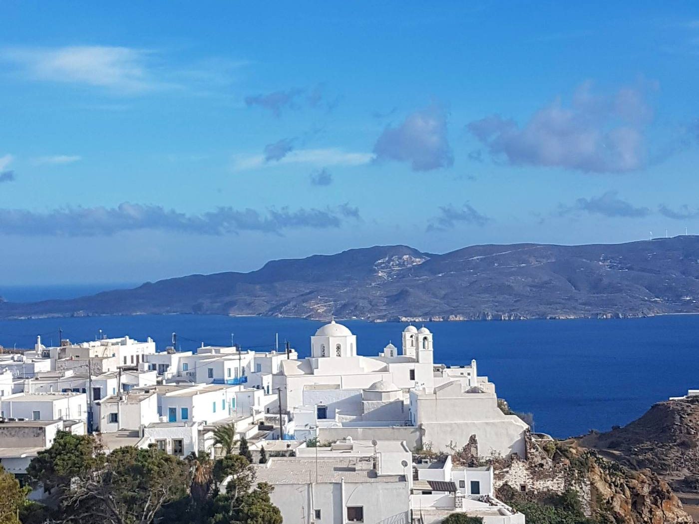 Plaka's whitewashed houses and the church of Panagia Thalassitra above Milos Bay in golden late-afternoon light