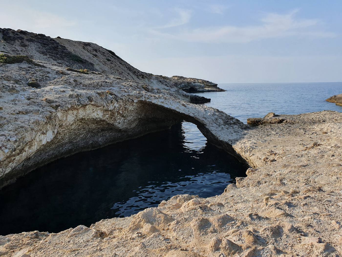 A narrow white rock cleft near Pollonia where the sea passes under a natural stone arch into a hidden turquoise cove