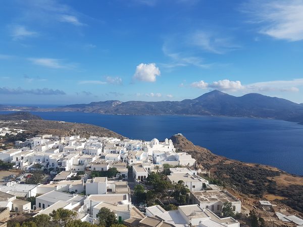 Whitewashed cubic houses of Plaka packed on the hilltop above the Gulf of Milos, with the domed Panagia Korfiatissa church on its terrace