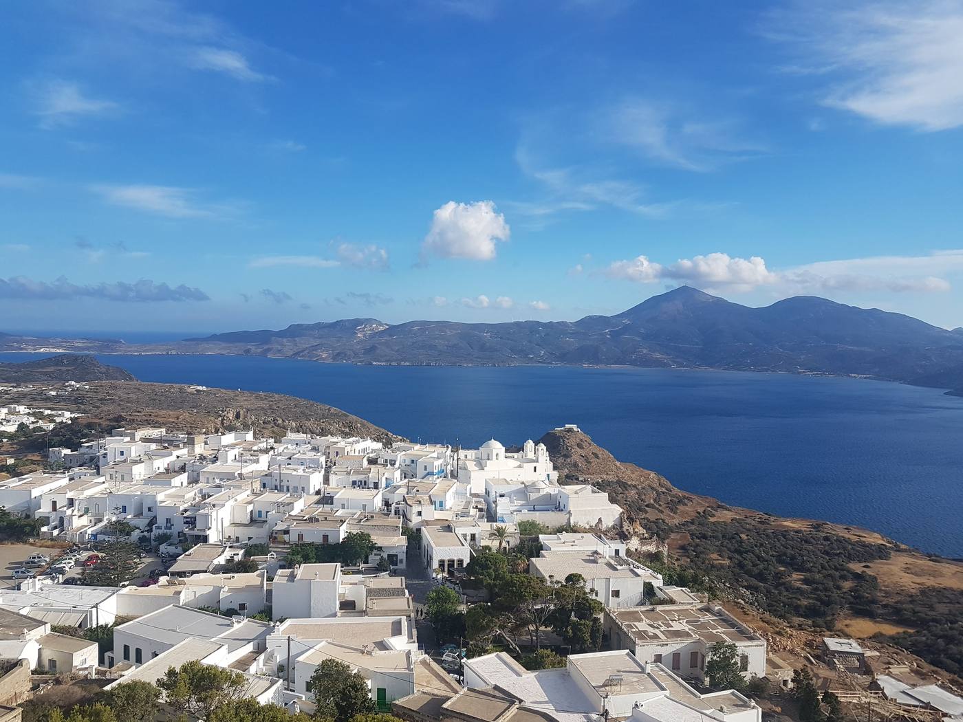 Whitewashed cubic houses of Plaka packed on the hilltop above the Gulf of Milos, with the domed Panagia Korfiatissa church on its terrace