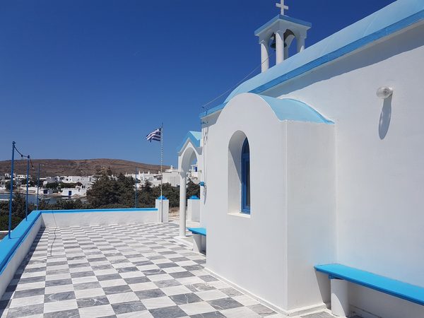 A chapel terrace above Pollonia with the Greek flag flying, looking down over the harbour, fishing boats and whitewashed village