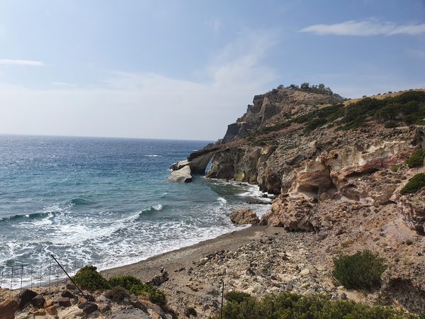 An empty cove on the wild southwest coast of Milos, a natural rock arch and bare headland with no development in sight