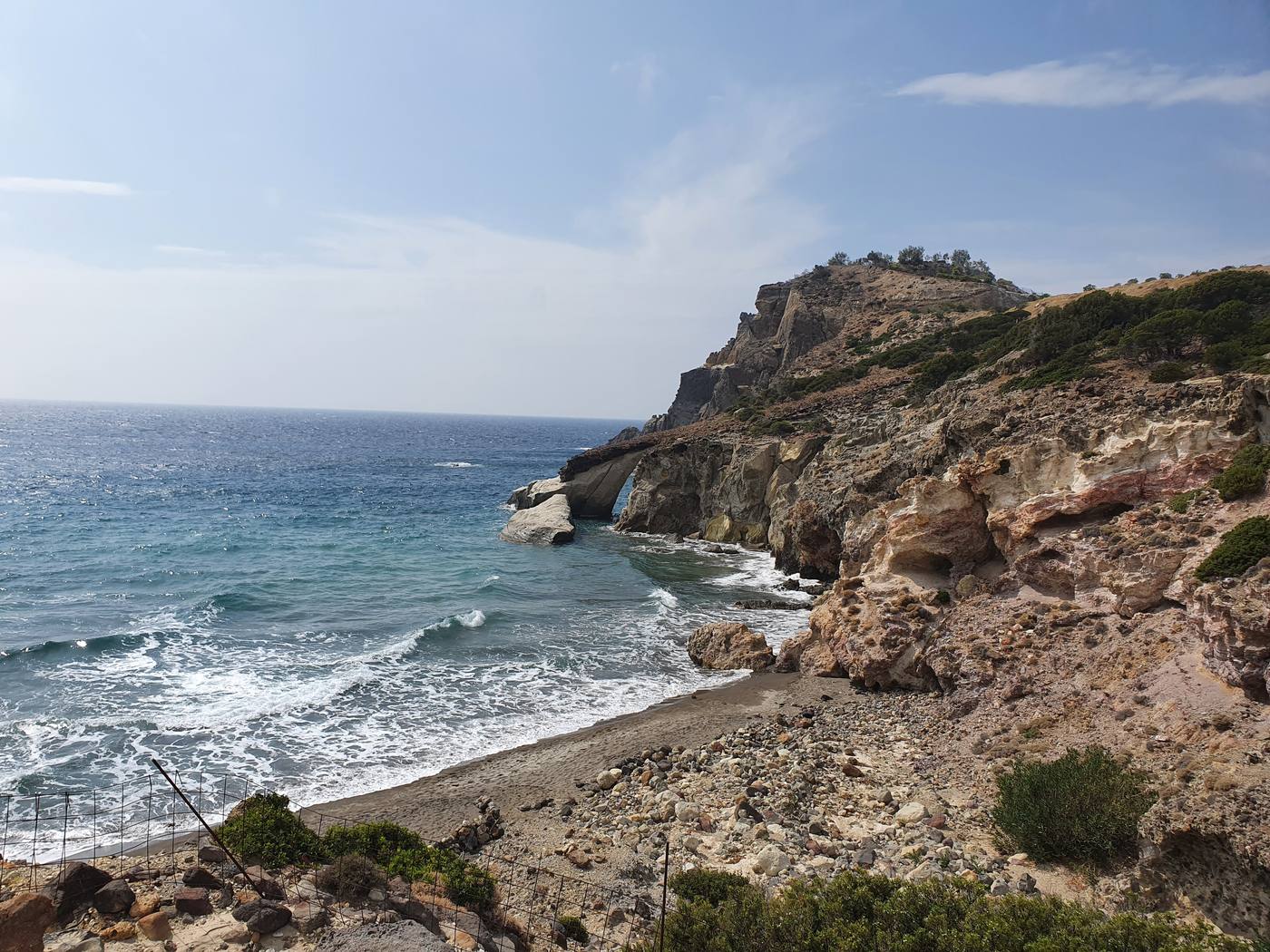 An empty cove on the wild southwest coast of Milos, a natural rock arch and bare headland with no development in sight