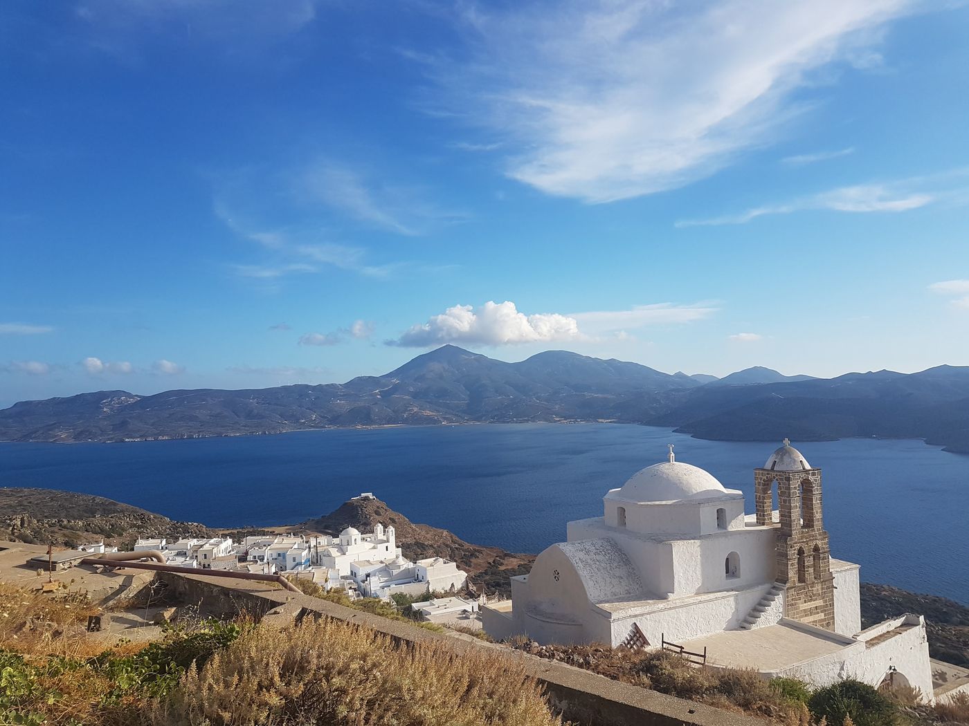 The whitewashed chapel and bell tower on the Kastro hill above Plaka, with the bay of Milos beyond